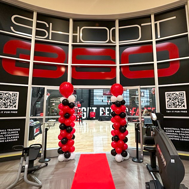 Shoot 360 facility entrance decorated with red, black, and white balloon columns beneath a large Shoot 360 logo, with the basketball court visible through the doors.